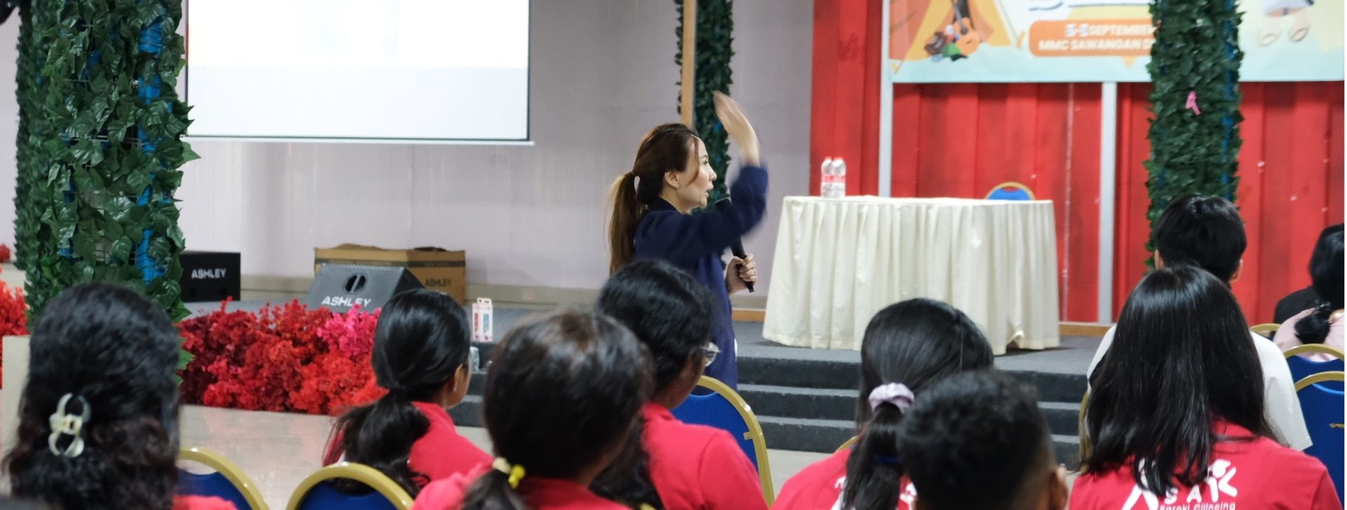 Pembicara sedang mempresentasikan materi di hadapan peserta berbaju merah