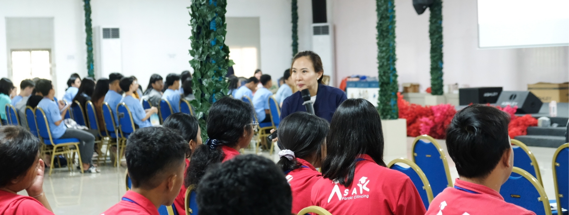 Pembicara wanita berbaju navy memegang mikrofon saat sesi presentasi